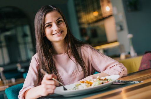 Portrait of a young girl at the restaurant having lunch. Smiling and looking straight into camera, blurred background.
